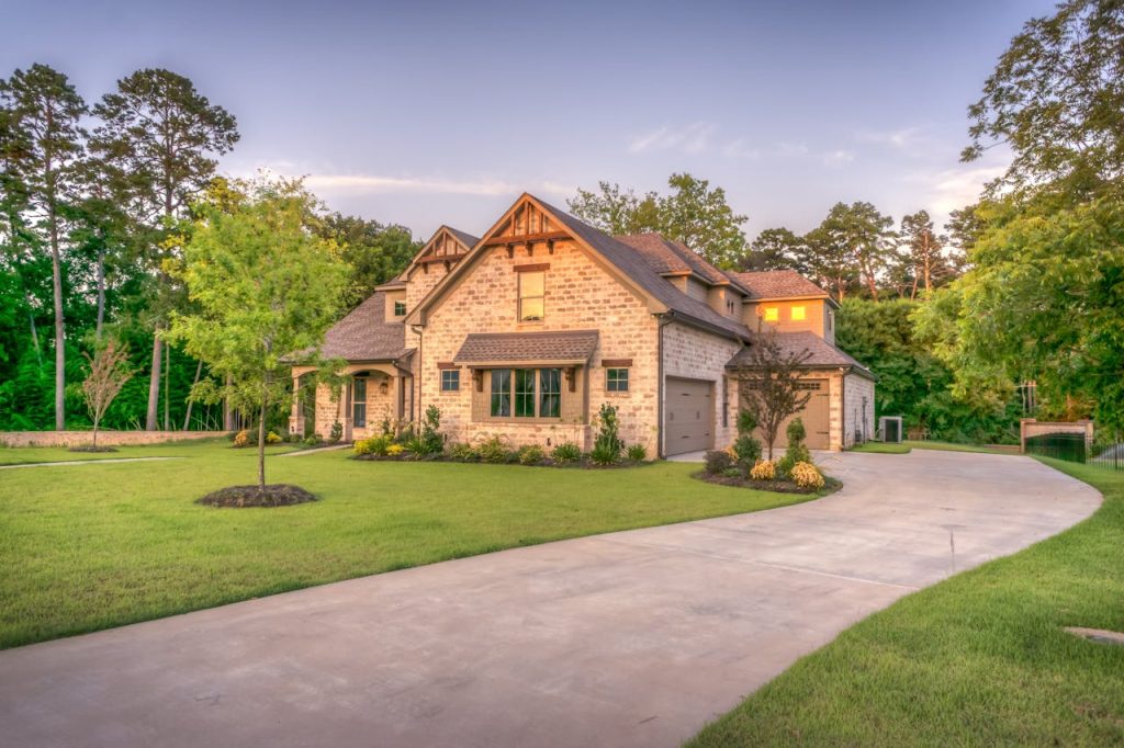 beige-bungalow-house-259588 Elegant stone family home surrounded by trees, lush lawn, and vibrant garden.